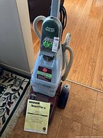 Front view of Hoover SteamVac upright carpet cleaner with attached user manual and bottle of cleaning solution.