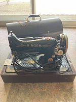 Front view of vintage Singer sewing machine on a wooden base with cord and hand crank visible, placed in front of a window.
