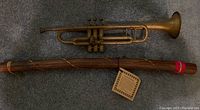 Photo showing the vintage trumpet and cactus rainstick on carpeted floor for overall lot view.