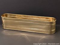 Side view of long narrow oblong shiny brass planter on black background showing smooth sides and rounded ends.