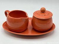 Front angle view of ceramic sugar bowl with lid and creamer on oval tray.