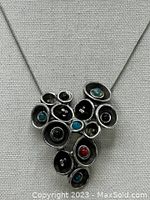 Front view of pewter cluster-shaped pendant with blue and red resin or glass stones on stainless steel chain against gray fabric background.