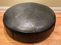 Front angle view of round leather patchwork ottoman on hardwood floor