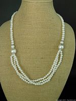Front view of vintage MCM pearl necklace on display bust, showing central three strand waterfall drop and silver-toned dividers.