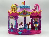 Front view of My Little Pony carousel with several pony figures positioned on and around it, showing the colorful design, blue heart slider and character figures.