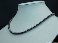 Full strand of dark gray/black pearls on display stand under lighting showing the necklace's length and lustrous finish.