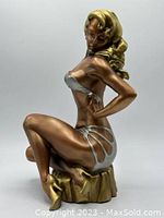 Side angle showing the figure seated with gold hair and silver swimsuit, gold heels, on draped base.