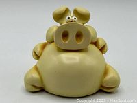 Front view of yellow fat piggy bank with bulging eyes and large nostrils, sitting with rounded body and limbs.