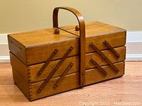 Front view of vintage wooden expandable sewing basket, closed with handle upright