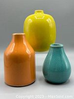 Image showing three colorful ceramic vases: tall orange vase, squat yellow vase, and pear-shaped turquoise vase against a gray background.