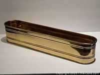 Long narrow shiny brass planter shown from side angle against plain background.