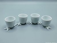 Set of four white glossy porcelain stoneware egg cups shaped like chicken feet with detailed toes forming the base, aligned in a row on a neutral surface