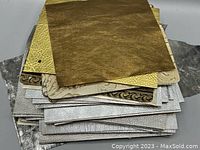 Stack of various metallic upholstery leather samples showing different textures and metallic shades of gold, silver, and copper.