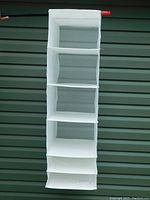 Full front view of the white IKEA SKUBB hanging organizer with six compartments against green background.