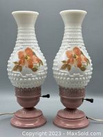Pair of vintage hobnail milk glass hurricane lamps with floral accents and pink metal bases, showing front view.