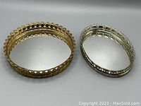 Both vanity trays side by side showing contrasting gold and silver scalloped metal rims and mirrored bases