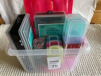 Overview of multiple plastic containers and boxes inside a clear plastic bucket with a red lid.