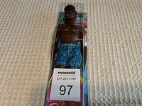 Front view of Barbie Ken doll in packaging wearing blue leaf print swim shorts, packaged with tropical background.