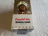 Front view of Campbell Kids bobble head doll in original box showing figure's face and upper body with chef's hat and red outfit.