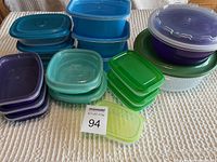 Various plastic kitchen containers in blue, green, purple, yellow, and white with lids, arranged on a textured surface.