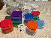 Photo showing multiple small plastic kitchen containers with colorful lids and clear bases.