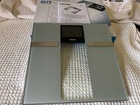 Scale placed on fabric surface showing its glass platform, metal electrodes, and digital display with Beurer branding.