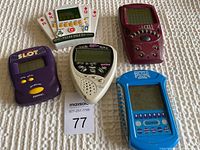 Top-down view of five vintage handheld electronic games arranged in a group on a white textured surface.