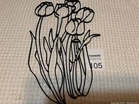 Black wrought iron hanging flowers wall art piece laid on textured fabric background, showing six hanging flowers with stems and leaves.