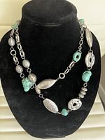 Front view of vintage silver-tone and turquoise bead necklace displayed on black bust showing assorted bead shapes and chain link details.