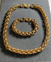 Full view of the vintage chunky rope braided gold-tone chain necklace and bracelet set laid flat on a grey surface.