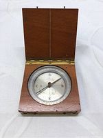 Open mahogany case showing the compass dial with cardinal directions and needle pointing.