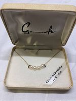 Top-down view of necklace with 5 cultured pearls on a gold chain inside the Genosart box