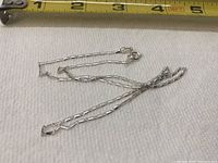 Silver necklace approximately 9 inches long with lobster claw clasp on white background and measuring tape.