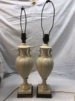Front view of both cream ceramic table lamps with ornate handles and square bases.