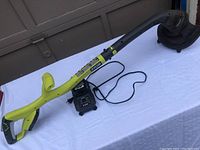Ryobi grass trimmer with curved yellow handle and black cutting head placed on a white surface with charger.