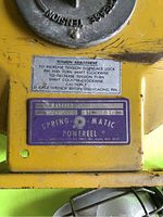 Close-up of Spring-O-Matic label with model number and tension adjustment instructions on yellow metal housing.