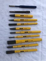 Photo of 11 Stanley punch and chisel tools laid out flat on a white surface showing yellow handles and metal tips with size markings