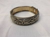 Vintage silver-tone hinged bangle bracelet showing detailed raised cherry and leaf motifs with white enamel background and open clasp mechanism.