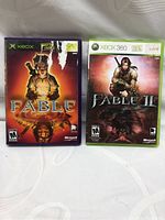 Photo of two Xbox game cases: Fable for Xbox and Fable II for Xbox 360 showing front cover art and ESRB ratings.