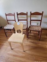 Four chairs displayed in a row: three traditional wood chairs with woven seats and one modern light wood chair in front.