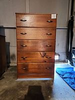 Front view of 5 drawer wood dresser showing medium brown wood finish and metal handles.
