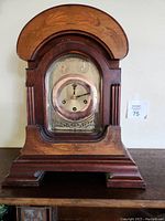 Front view of antique wooden mantle clock with glass front door and round clock face inside a brass bezel.