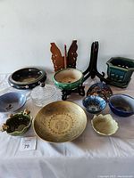 Full view of the lot showing variety of bowls, brass bowl, wooden stands, and ceramic planters on a white cloth