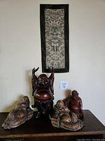 Overall photo showing four wood carved Buddha statues arranged on a flat surface with an embroidered Chinese scroll hanging above them.