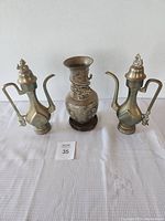 Three bronze pieces (vase center, two ewers sides) on white cloth showing overall lot arrangement