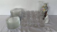 Photo showing stacks of clear glass plates and a group of clear crystal stem glasses, along with various vases including a floral-patterned ceramic one.