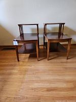Front view of two wooden end tables side by side showing rectangular tabletops and smaller raised shelves.
