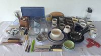 Wide shot of all kitchen items on a table including plates, mugs, glassware, cutlery, and utensils.