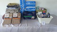 Full lot view showing stacked linens, brownstone panel drapes, men's underpants pack, medical items in bin and basket, and boxed razors.