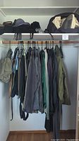 Closet view showing assorted men's clothing hanging on wooden rod, hats and scarves on shelf above